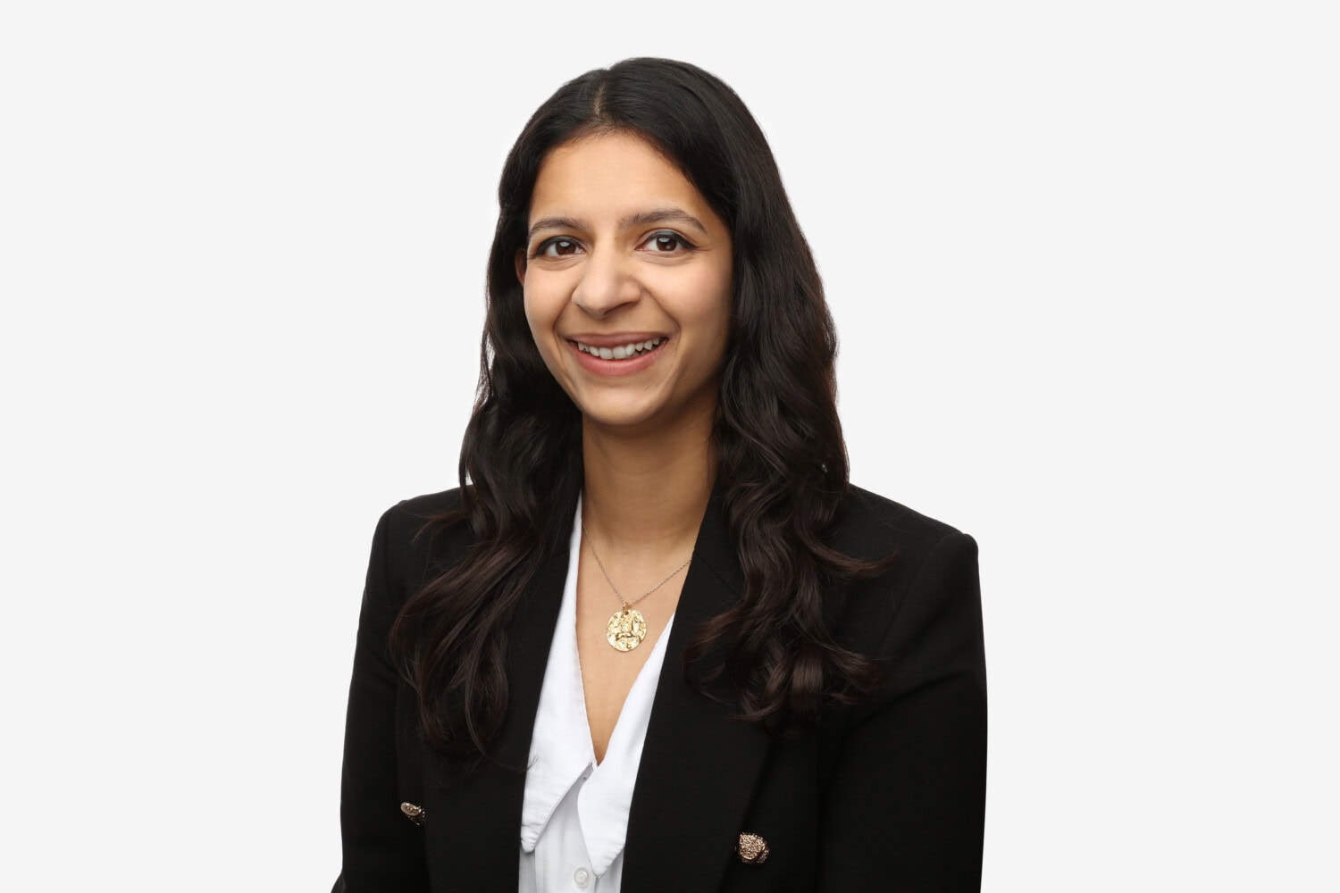 Ashvika Dalmia, a woman with long dark hair, wears a black blazer and white blouse, smiling in front of a plain white background.