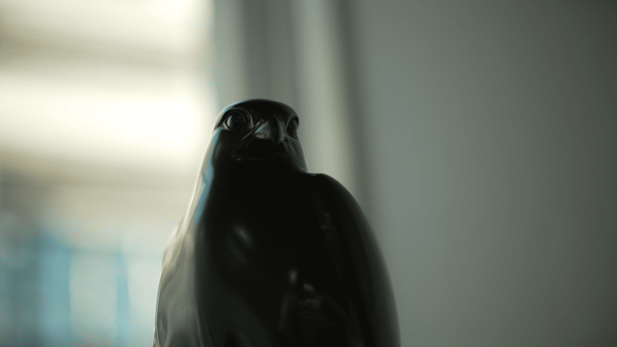 Close-up of a black bird statue with a blurred background, reminiscent of Stan Miranda's artistic touch. The bird's head is tilted slightly, facing forward.