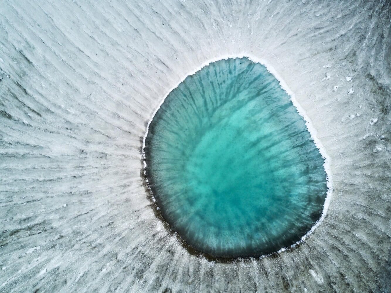 An aerial view reveals a circular turquoise lake amidst snowy terrain, resembling an eye, offering insights into 2025's important environmental trends.