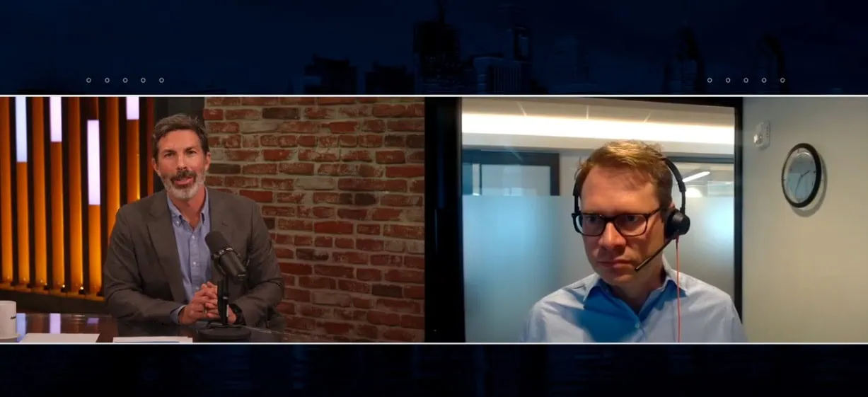 Two men engage in a split-screen video call. The man on the left, perhaps a Chief Investment Officer, sits in a studio with a brick wall backdrop, while the man on the right wears a headset in an office. A clock graces the wall as they discuss insights likely for Partners Capital or Dakota Live! Podcast.