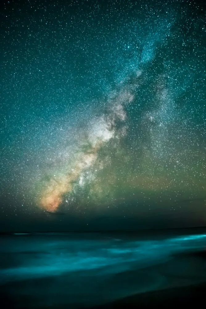 A vibrant display of the Milky Way galaxy stretches across the night sky above a calm, blurred body of water, offering celestial insights similar to those gathered in 2021.