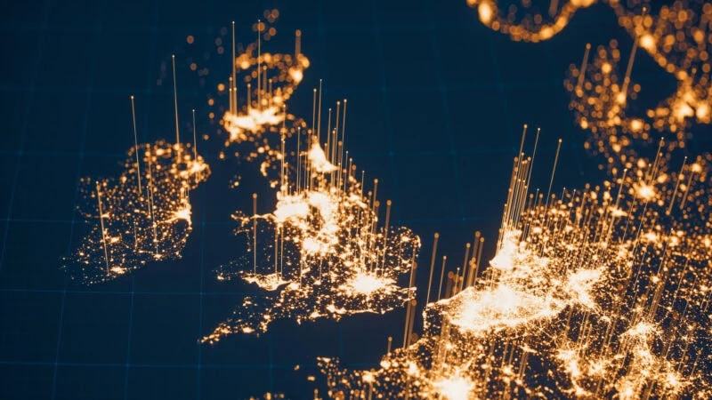 A digital map highlighting population density in the UK and Western Europe with bright yellow lights and vertical lines on a dark blue background.