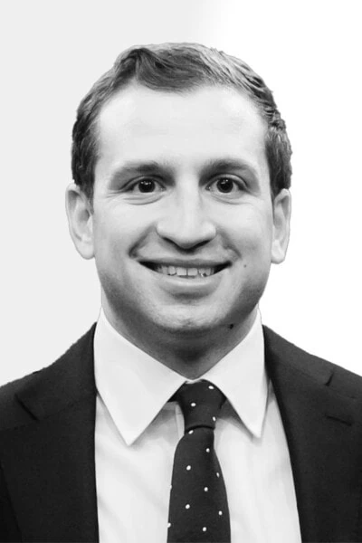 Joe Mason, a man in a business suit with a polka dot tie, is smiling directly at the camera against a plain background.