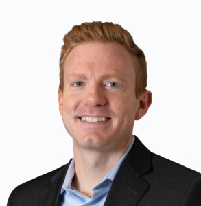 Kevin Widmaier, a man with short reddish-blond hair, wears a dark blazer and light blue collared shirt, smiling at the camera against a plain light background.