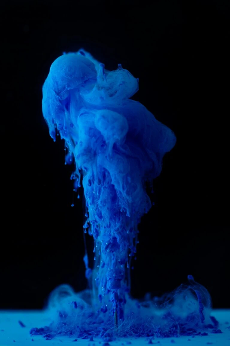 Vivid blue paint cascades and drips in a fluid, abstract form against a black background, creating an artistic playbook that defies the recession of creativity.