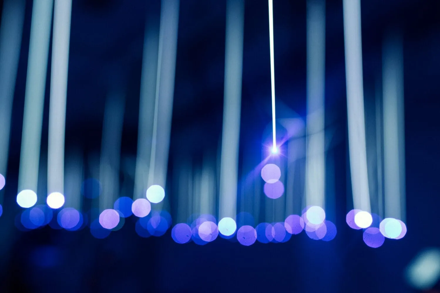 Abstract image showing vertical light beams and out-of-focus blue circular bokeh lights against a dark background, reminiscent of the technological advancements and dynamic shifts discussed in Insights 2014.