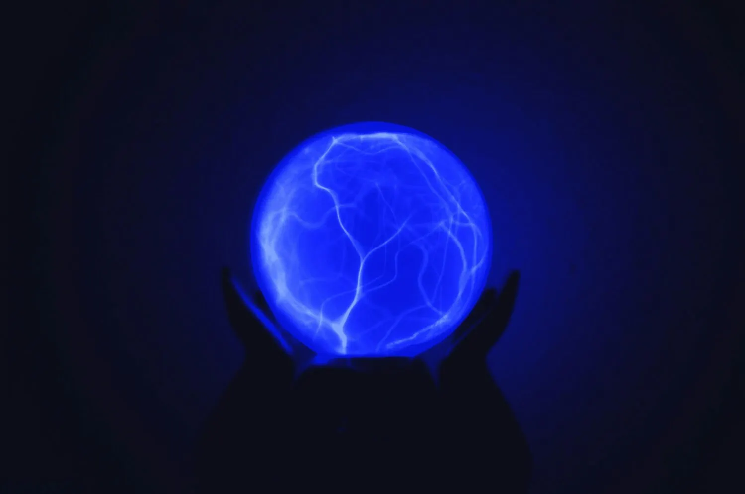 Hands holding a glowing blue plasma ball emitting electric currents on a dark background, mirroring the complexities of Portfolio Risk management.