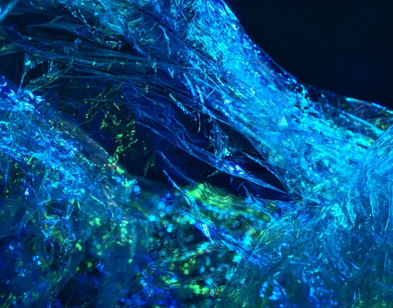 Close-up of crinkled, translucent blue and green plastic with light reflecting off its surface, creating an abstract, shimmering effect that mirrors our investment philosophy.