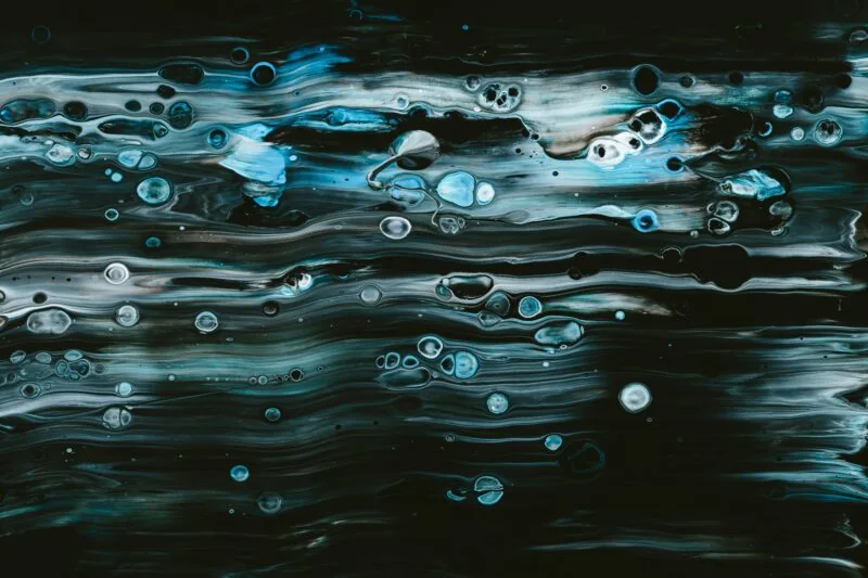 Abstract artwork featuring fluid, swirling patterns in shades of blue, black, and white, with bubble-like shapes scattered throughout—evoking the dynamic energy seen in Partners Capital's 2022 Report on Sustainable Investing.