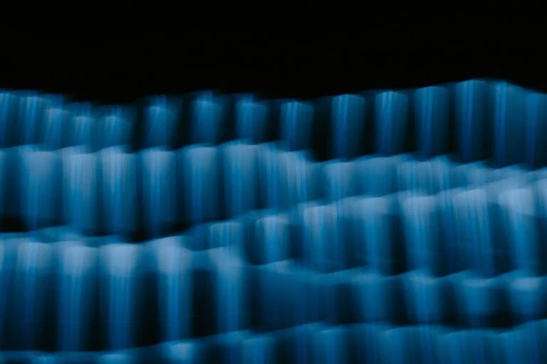 Abstract image of rows of wavy blue light streaks against a dark background, evoking the complexity and dynamism of portfolio management.