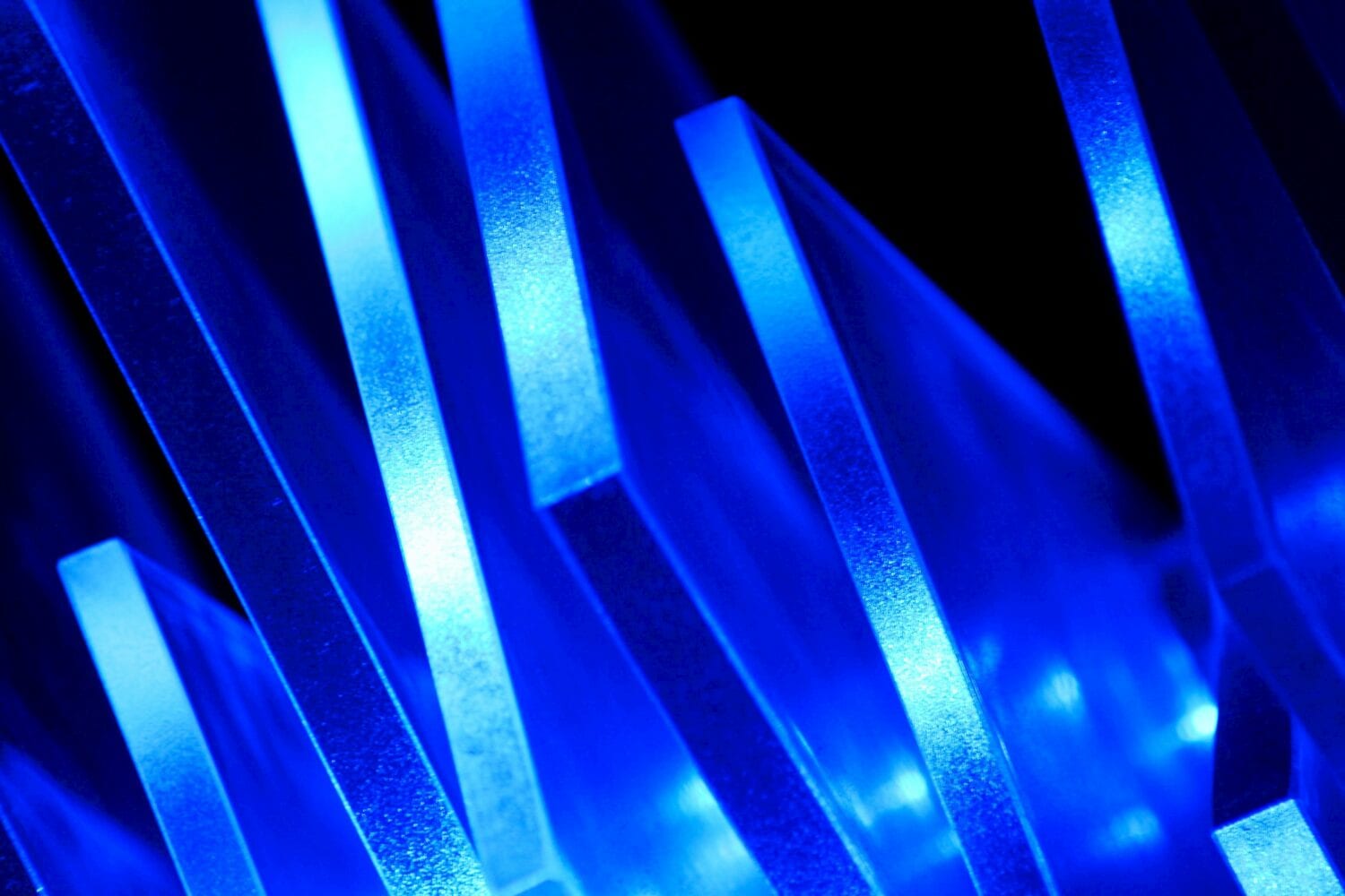 Close-up of vertically aligned, luminescent blue acrylic sheets creating a layered, abstract visual pattern against a dark background, reminiscent of emerging investment themes for 2023.